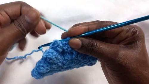 Hands beginning a small blue granny square center with a teal hook on a white surface.
