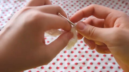 Hands pulling white yarn through a small loop on a silver crochet hook at the very start of a foundation chain.