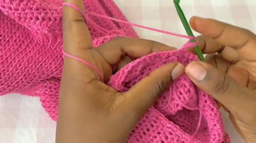 Pink crochet sweater fabric being joined at the shoulder seam with a green crochet hook