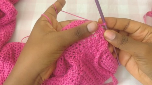 Open stitch rows of pink crochet fabric being worked at the neckline edge with a purple hook