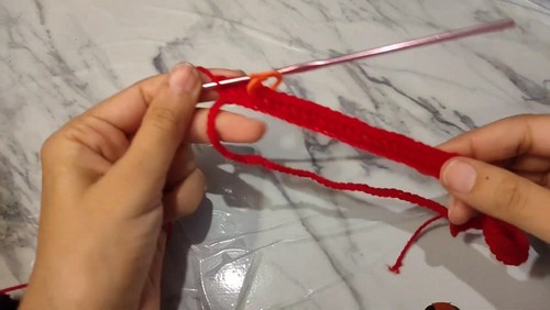 Hands working a red foundation chain on a marble surface with a pink crochet hook