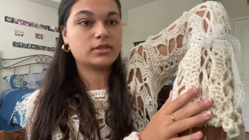 Creator holding up the assembled cream lace crochet sweater showing the open motif body and flared sleeve construction