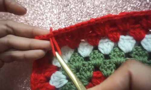 Working a red joining round along the edge of the green and white granny square panel with a gold hook