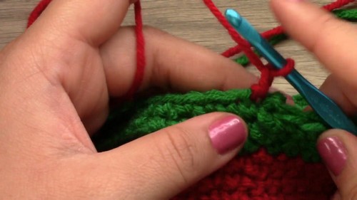 Joining green yarn to the red body of the dog sweater with a blue hook to begin the first stripe