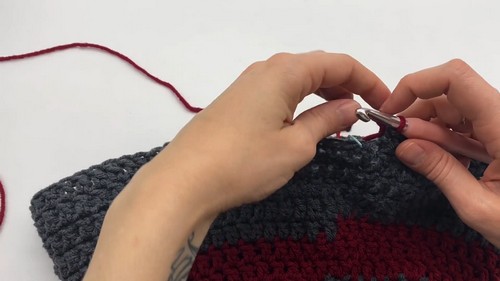 Joining red yarn to the grey and red striped dog sweater body with a metal hook