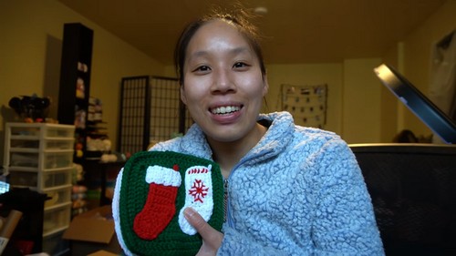 Holding two finished crochet squares, a red and white stocking on green and a red snowflake on white, before joining