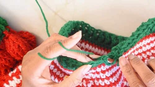 Joining the green ribbed cuff to the red and green sleeve section with a white yarn needle
