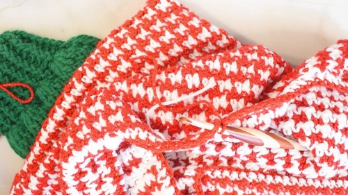 Close view of the red and white houndstooth body fabric with a pink handled hook resting on the edge